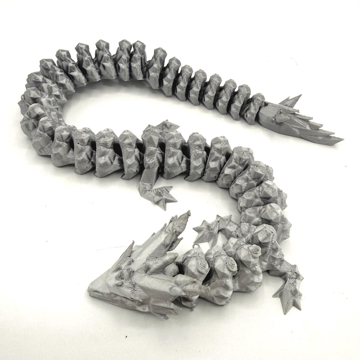 A silver 3D-printed articulated fantasy creature or dragon-like monster, shown coiled on a plain white background.