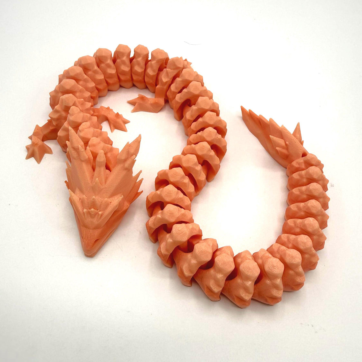 An orange 3D-printed articulated dragon toy, coiled on a plain white background.