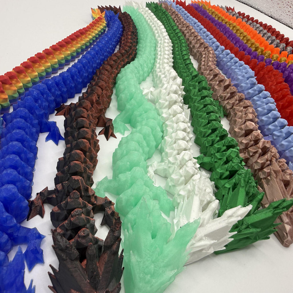A series of long, ribbed, dragon-like sculptural objects arranged in a fan shape on a white surface, shown in many different colors including rainbow, blue, brown, mint green, white, forest green, tan, red, orange, purple, and blue.