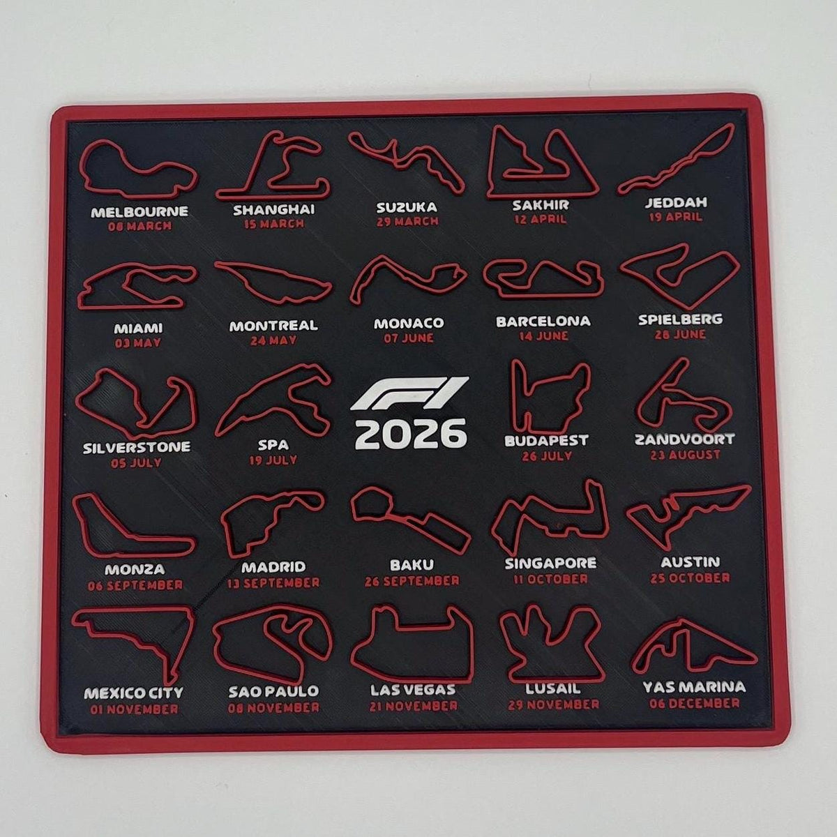 A square black F1 2026 racing calendar mat with a red border, featuring 2026 Formula 1 race tracks and circuits in red and white.
