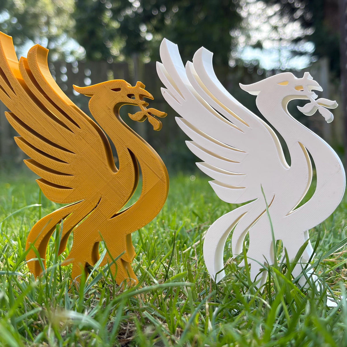 Two 3D printed bird-shaped football fan art, one golden yellow and one white, standing in green grass outdoors.