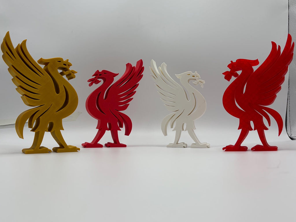 Four 3D-printed Liverpool bird figurines in gold, red, and white, arranged in a row against a white and grey backdrop.