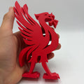 A red Liverpool FC crest figurine held in a person's hand against a plain white studio background.