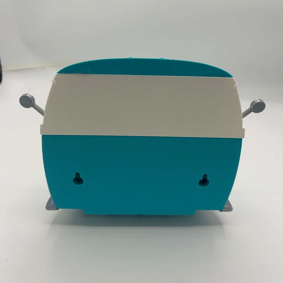 A retro-style turquoise and white plastic key holder with small grey side knobs and feet, photographed against a plain light grey background.