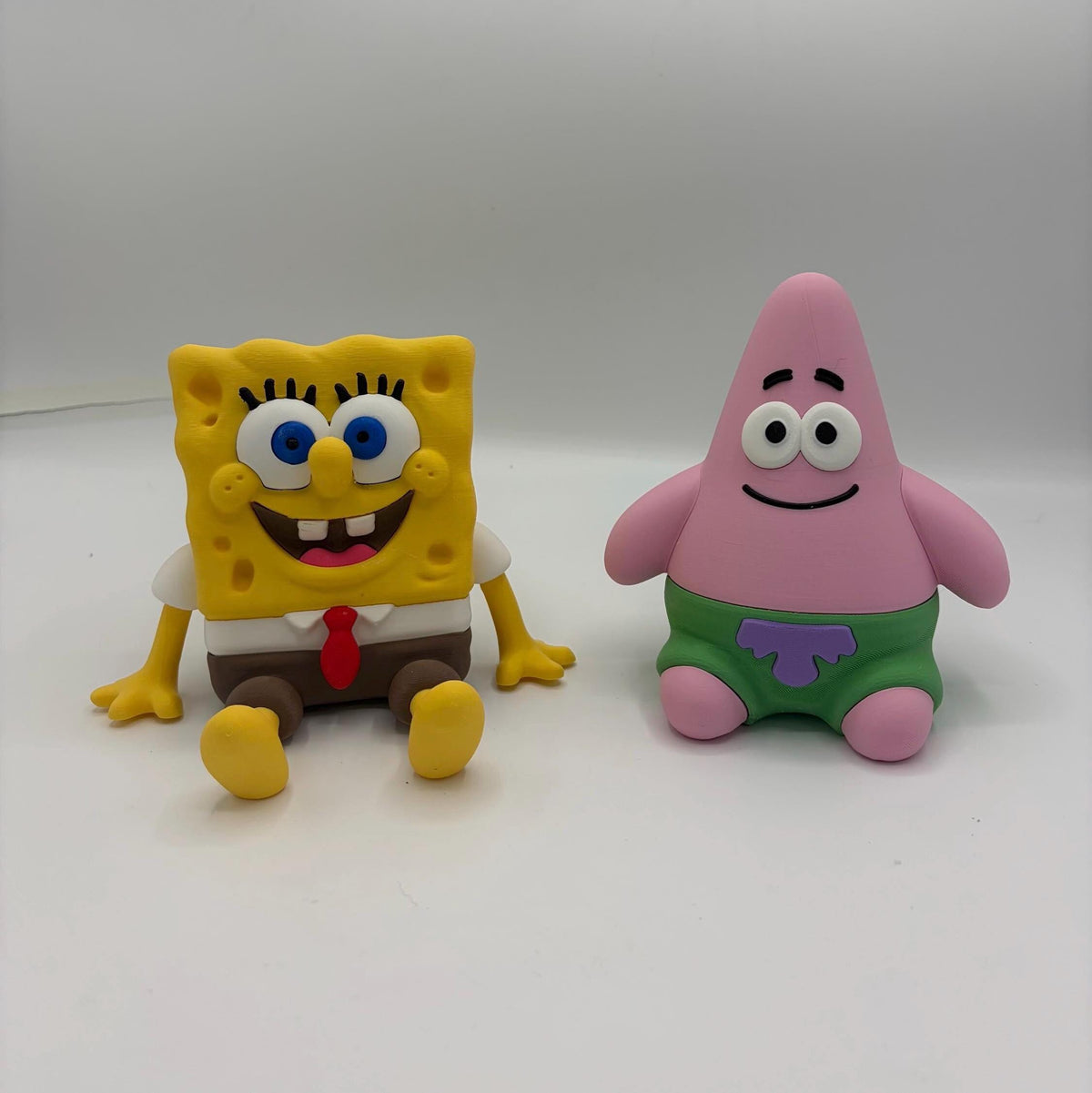 Two cartoon figurines, SpongeBob SquarePants and Patrick Star, shown side by side on a plain light grey studio background.
