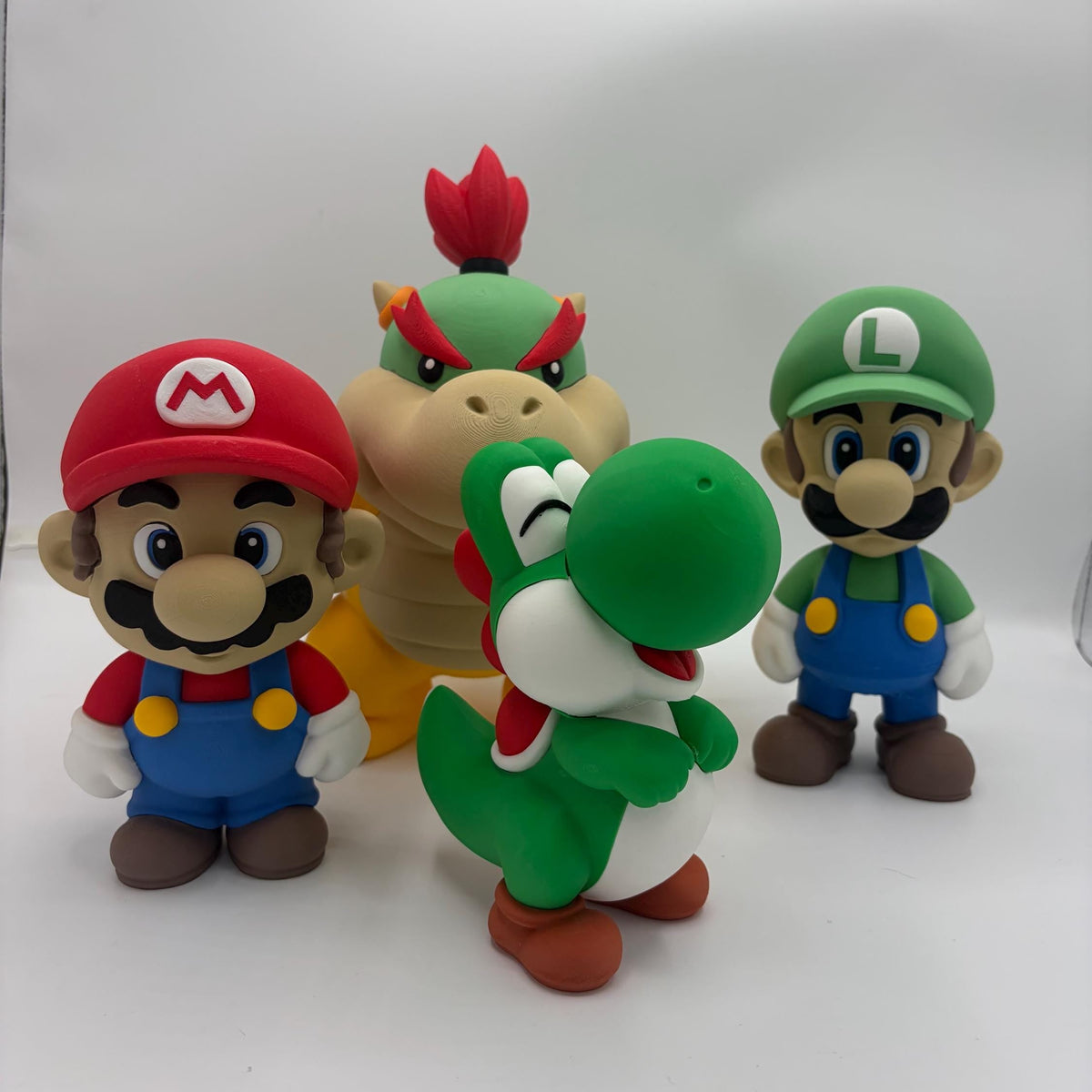 Four Super Mario character figurines, including Mario, Luigi, Yoshi, and Bowser, displayed on a white studio background.