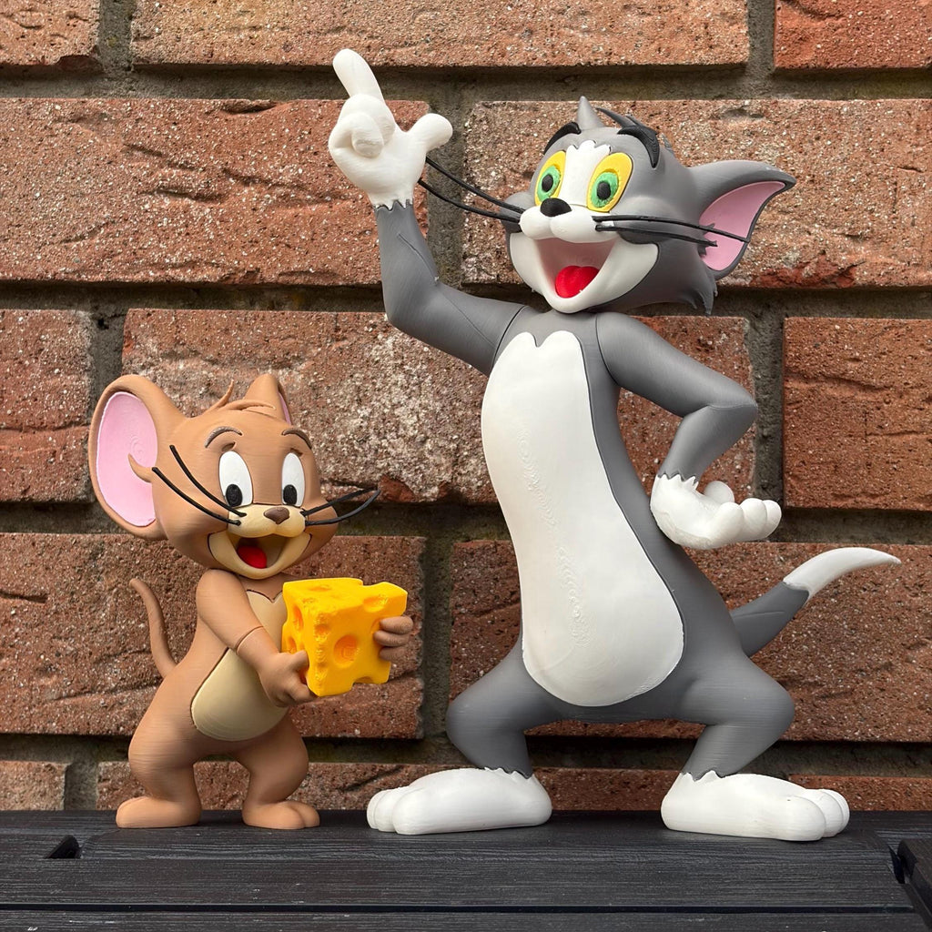 A collectible figurine of Tom and Jerry the cartoon characters posed in front of a red brick wall. Tom is grey and white, pointing upwards, while Jerry is tan and holding a yellow cheese block.