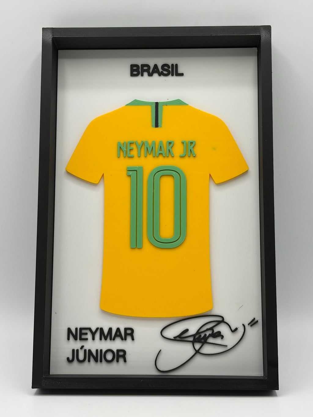 A framed Neymar Jr. Brazil jersey display with a yellow soccer shirt, green trim, the number 10, and black text reading BRASIL and NEYMAR JÚNIOR, plus a signature on a white background inside a black frame.