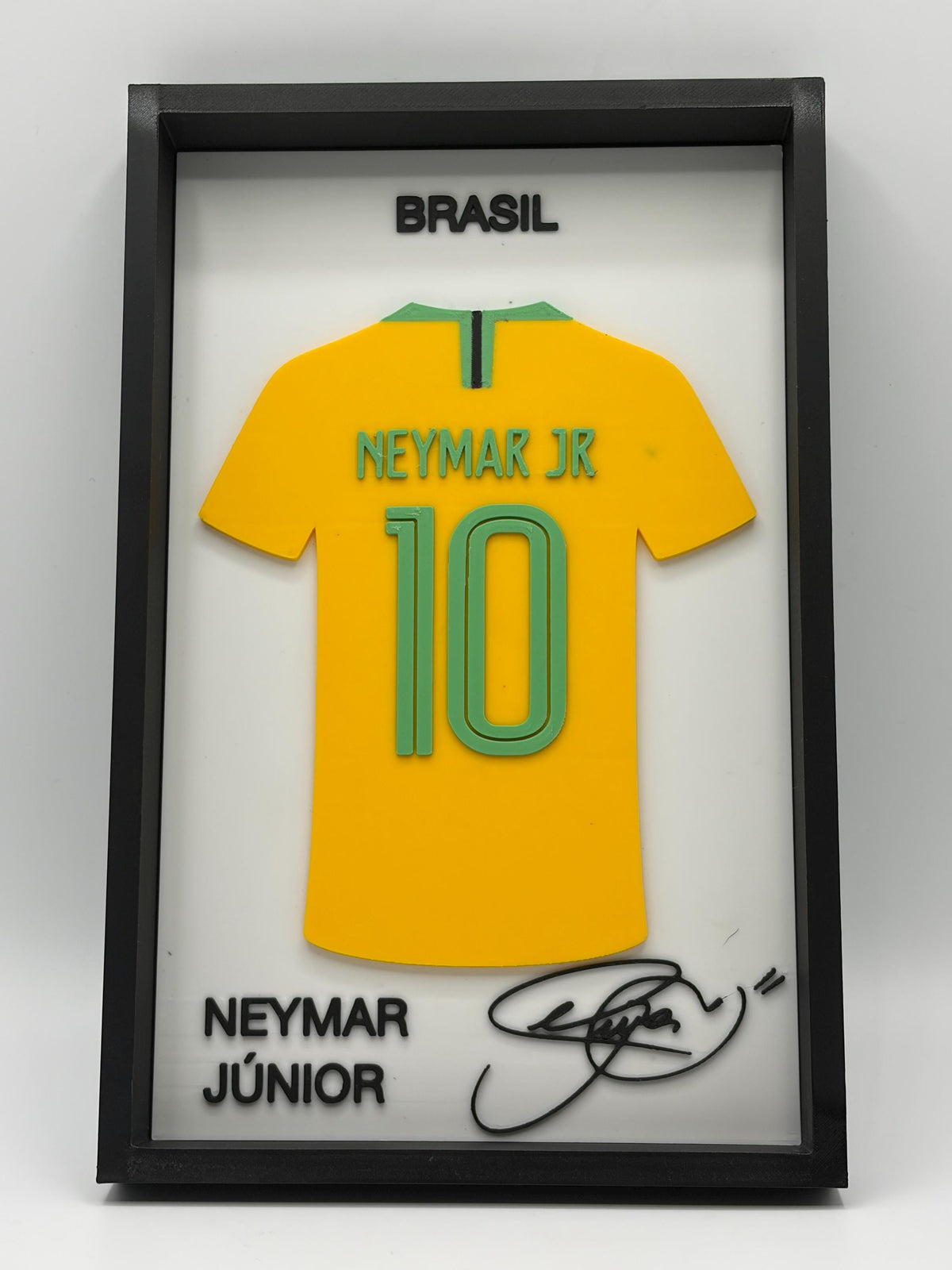 A framed Neymar Jr. Brazil jersey display with a yellow soccer shirt, green trim, the number 10, and black text reading BRASIL and NEYMAR JÚNIOR, plus a signature on a white background inside a black frame.