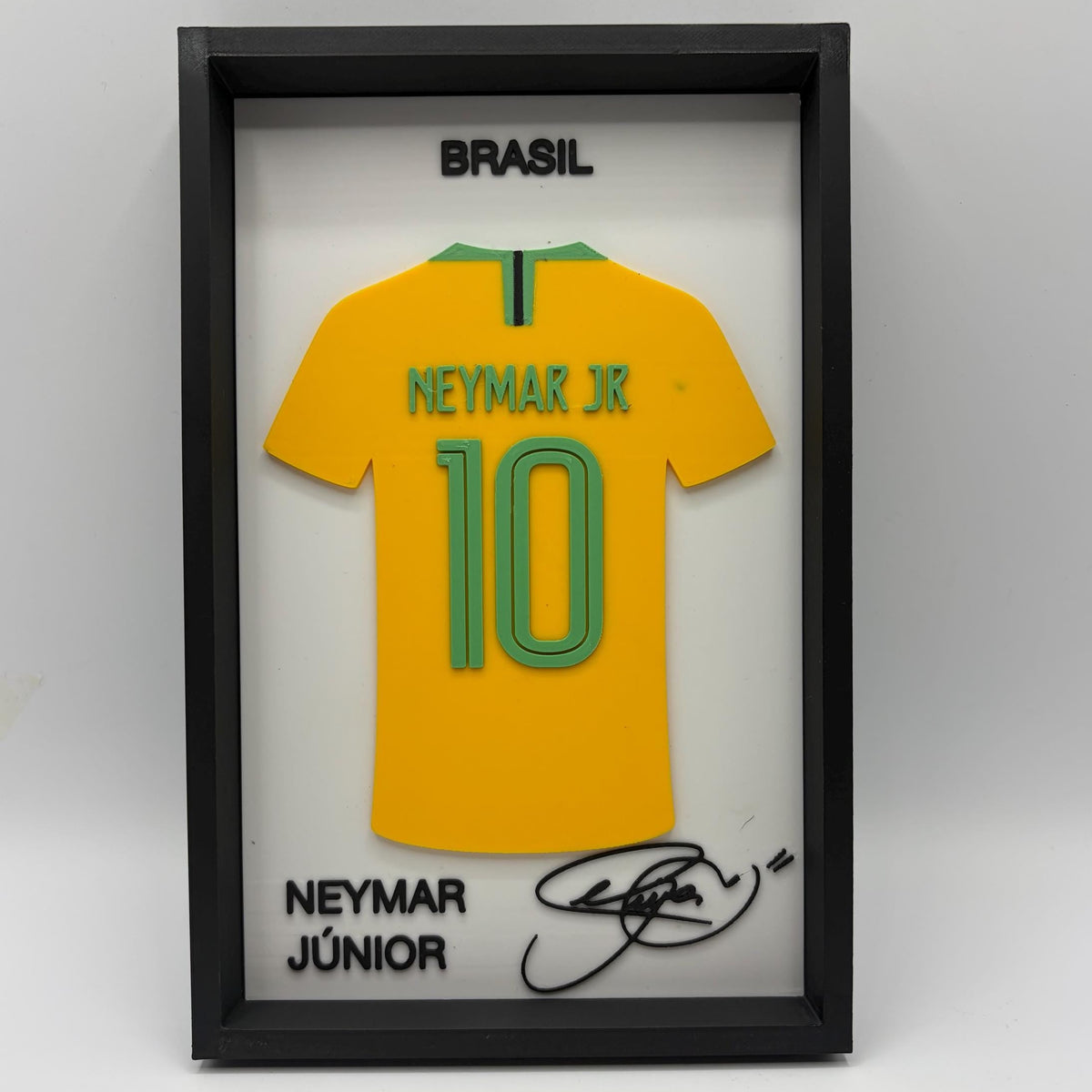 A framed display featuring a yellow Brazil soccer jersey with 'NEYMAR JR' and the number '10' on the back, inside a black shadowbox frame with 'BRASIL' at the top and 'NEYMAR JÚNIOR' plus a signature at the bottom.