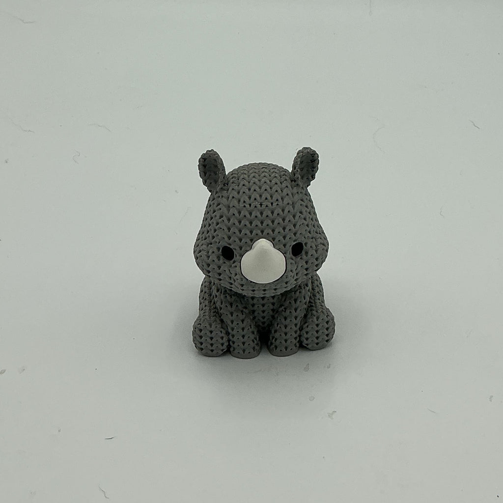 A small gray knitted-style rhino figurine sitting on a plain light gray surface against a matching gray background.
