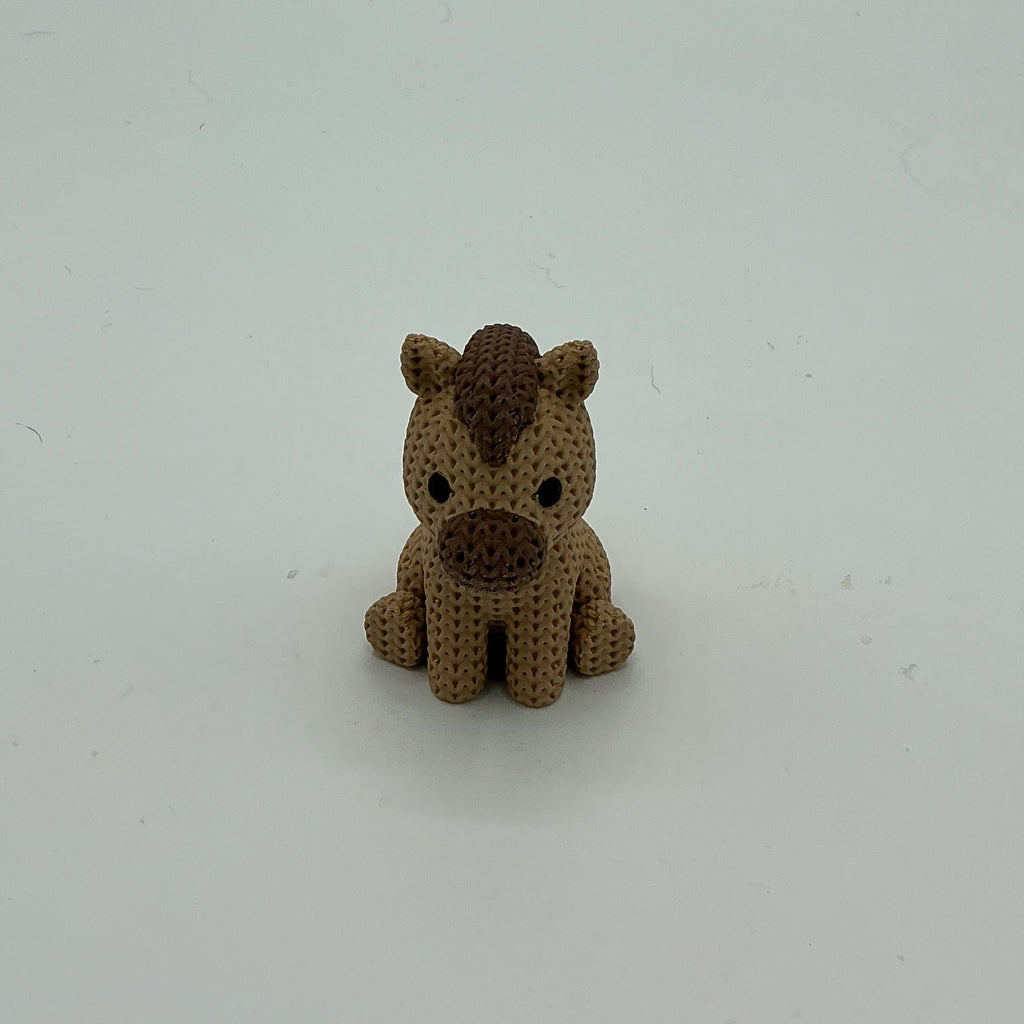 A small handmade crocheted-style pony figurine in light brown and dark brown, sitting on a plain light gray background.