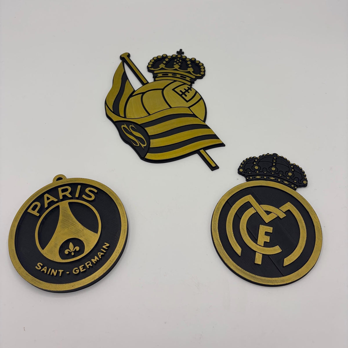 Three Paris Saint-Germain FC themed stickers or decals on a plain white background: a circular PSG emblem, a central crest with a crown and flag, and a circular Real Madrid-style FC logo.