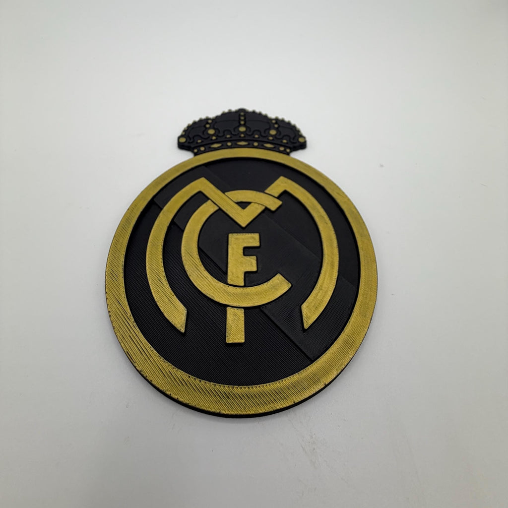 A circular black and gold FC logo patch with a small crown detail on top, displayed on a plain white surface.
