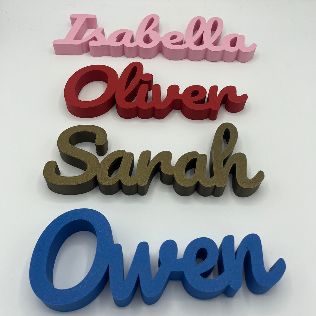 Four personalised name plaques in different colours stacked vertically on a white background: pink 'Isabella', red 'Oliver', bronze 'Sarah', and blue 'Owen'.