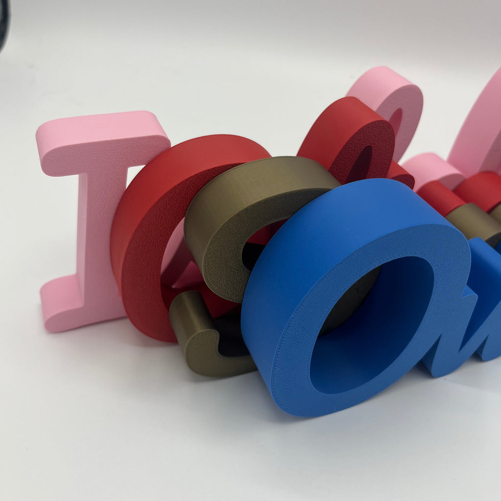 A pile of colourful 3D printed letters spelling various names on a white studio background.