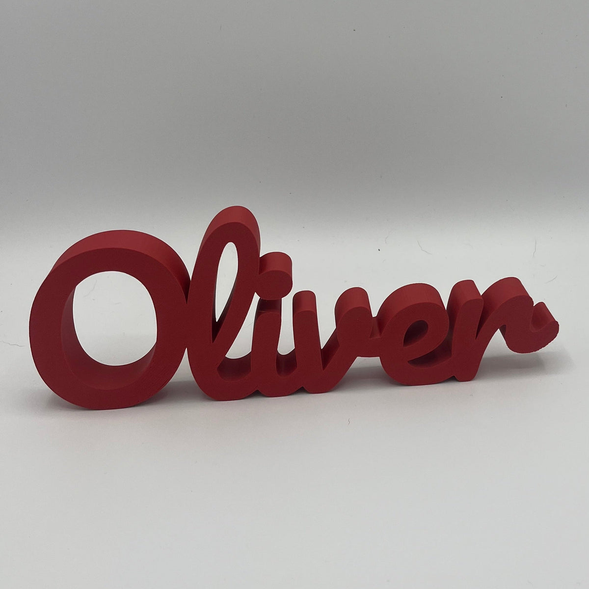 A red 3D custom name sign spelling 'Oliver' in a cursive font, displayed on a neutral gray background.
