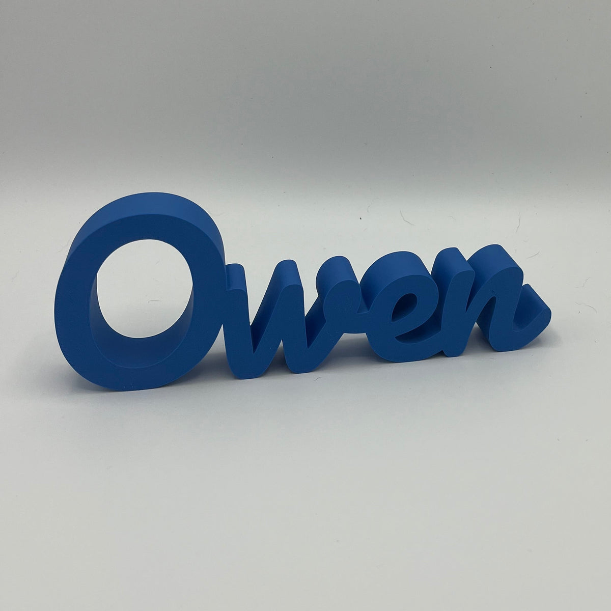 A blue 3D name cutout spelling 'Owen' in cursive, displayed on a neutral grey background.