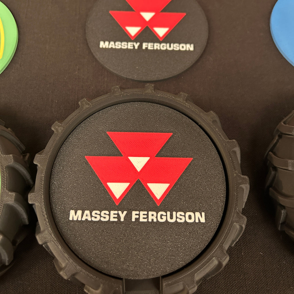 A close-up of a black textured foam disc with a red and white Massey Ferguson logo and white brand text, shown on a dark surface with other colorful discs partially visible around it.