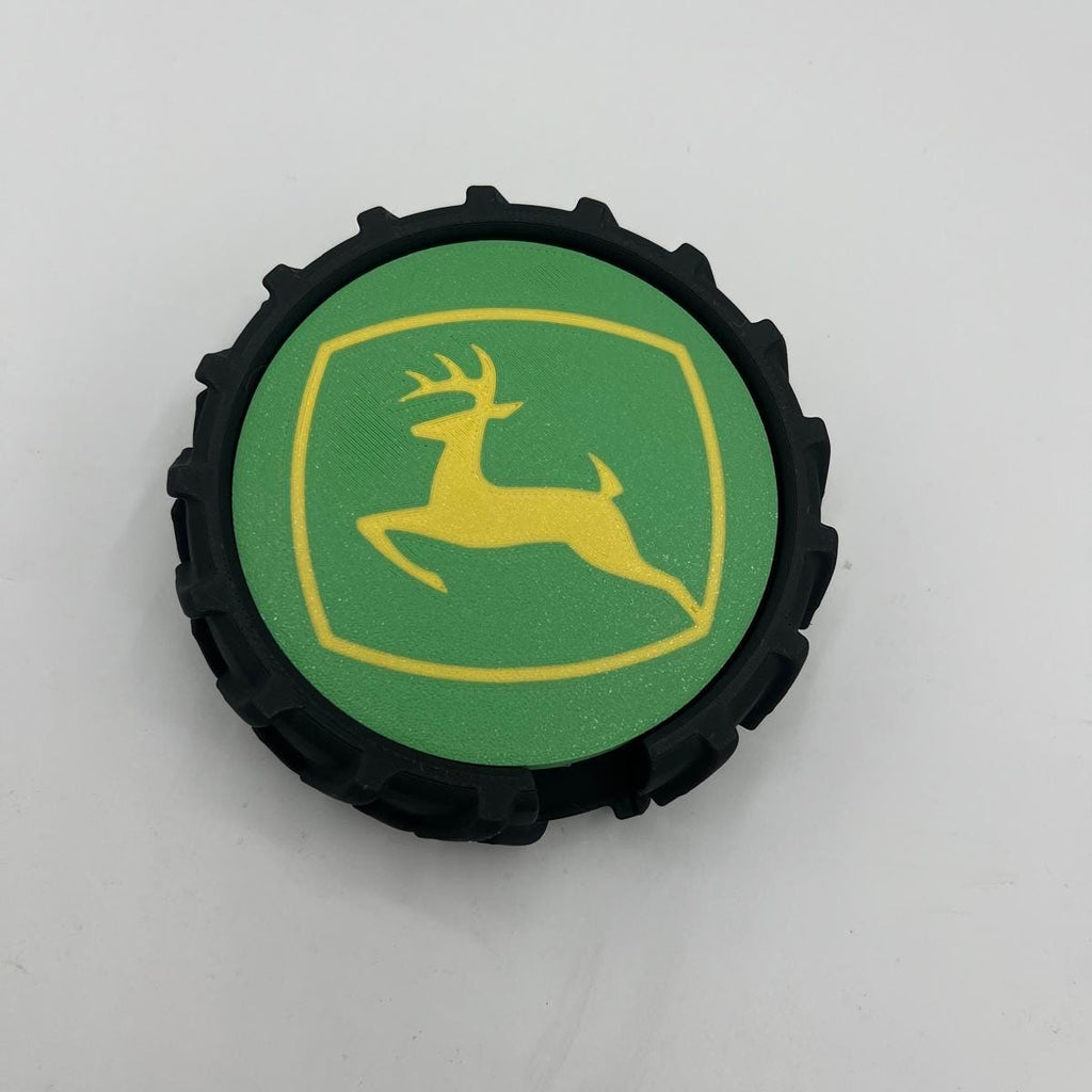 A circular black tyre with a green center featuring the yellow John Deere logo, photographed on a plain light background.