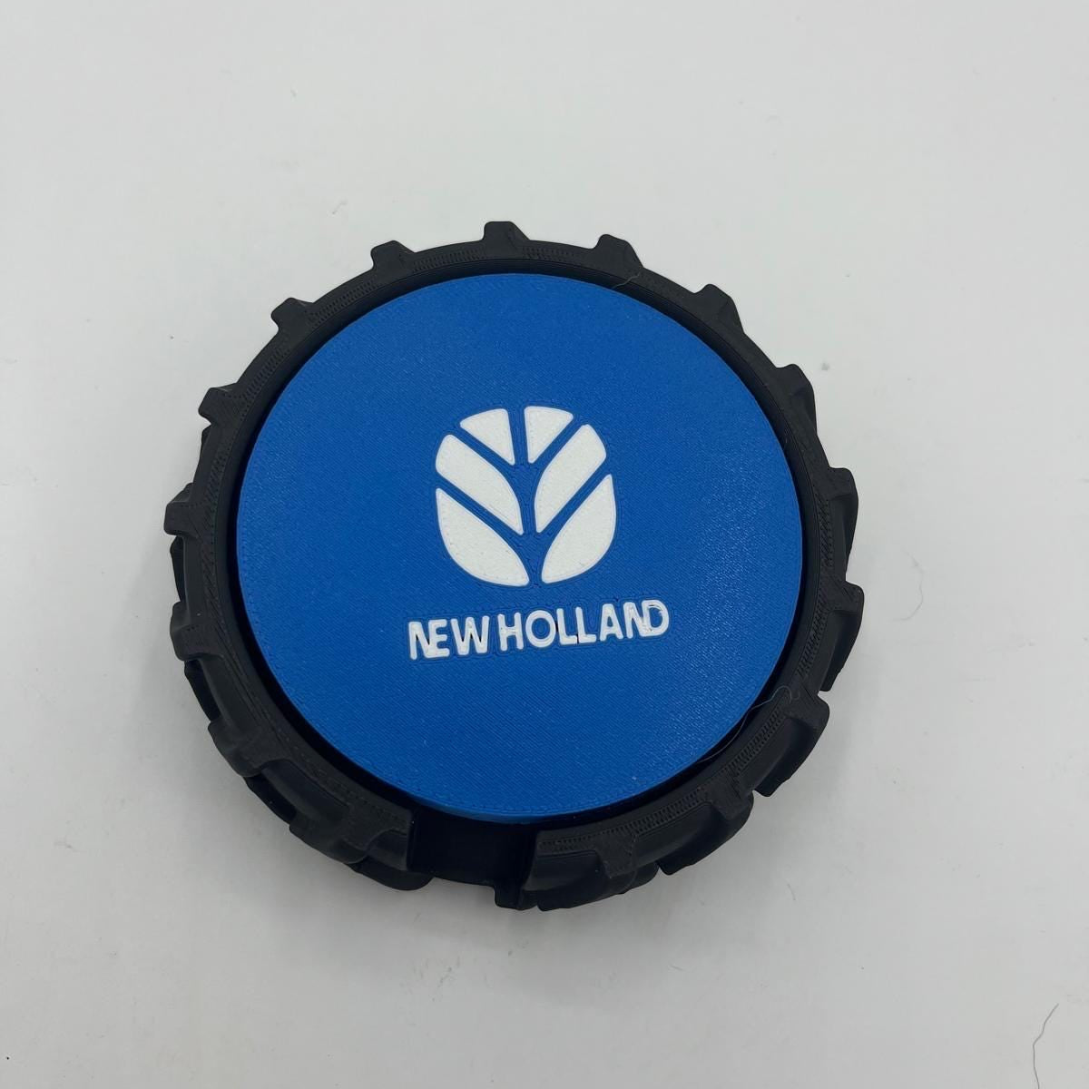 A circular black tyre with blue and white New Holland logo and brand name printed on the centre, shown on a plain light background.