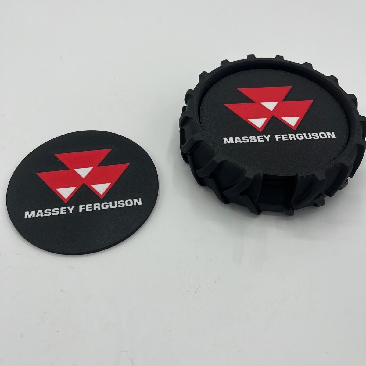 Two black circular coasters with the red and white Massey Ferguson logo and white 'MASSEY FERGUSON' text, shown on a light grey background.
