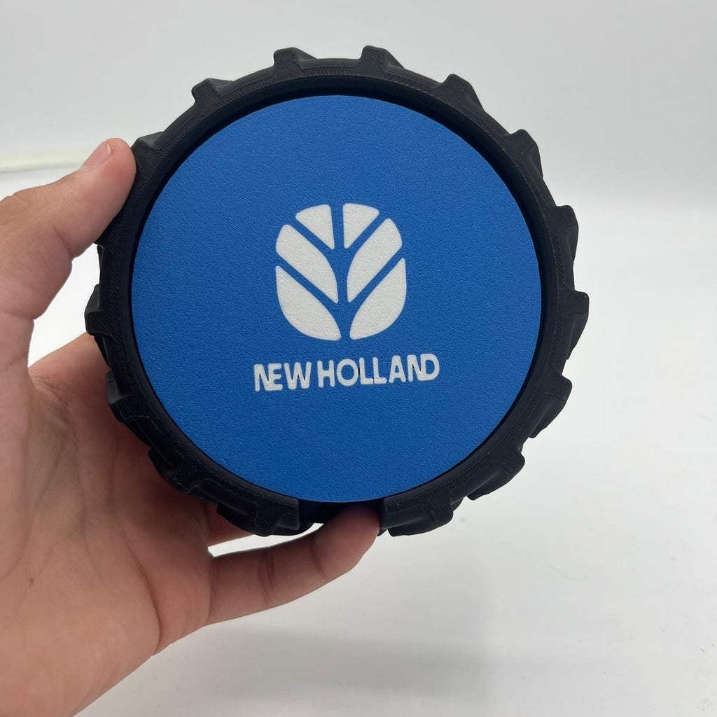 A hand holding a circular black tyre with blue and black New Holland coasters against a plain white background.