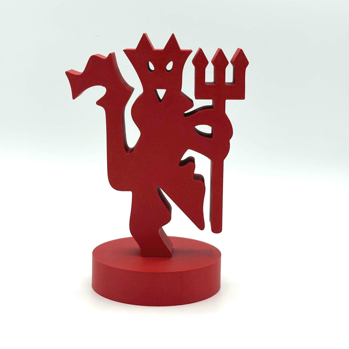 A red 3D-printed devil figurine standing on a matching round red base, set against a clean white studio background.