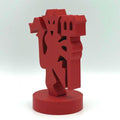 A red abstract geometric sculpture standing on a round cylindrical base, photographed against a plain light grey studio background.